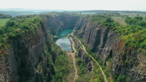 aerial: reveal shot and fly through a limestone canyon of an old quarry with turquoise lake and a small bridge