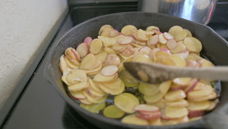 delicious potatoes fry in oil in cast iron pan, stirred with wooden spoon