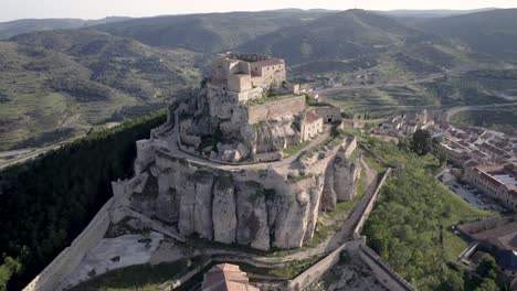 close aerial view of the medieval castle of morella on top of a rocky hill surrounded by green mediterranean pine trees in spain