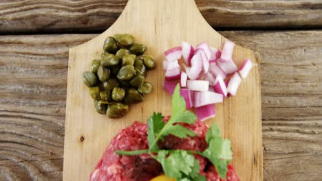 pâté de hamburger crue et ingrédients sur planche en bois