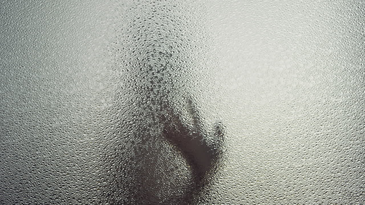 A female silhouette behind the frosted window touches the glass slowly