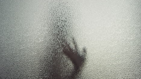 a female silhouette behind the frosted window touches the glass slowly