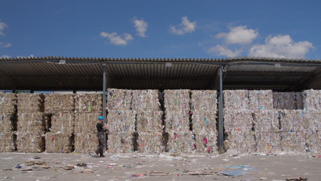 Gestapelte-Gepresste-Ballen,-Recyceltes-Altpapier-Unter-Deckung,-Vorbeigehender-Arbeiter