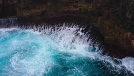 static aerial shot of intense blue waves crashing against the rocks of cliff
