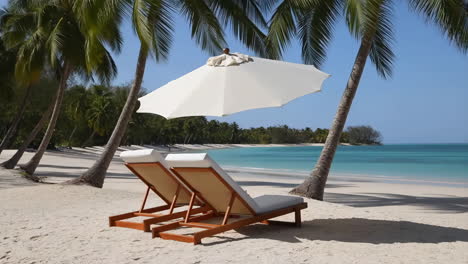 two empty lounge chairs on a tropical beach with palm trees and turquoise ocean