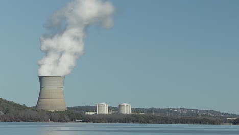 time lapse of a nuclear stack emitting steam on a sunny and cloudless day with lake in the foreground