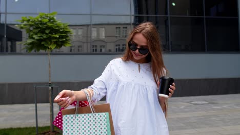 girl stay near mall with shopping bags and drinking coffee. satisfied and happy with purchase