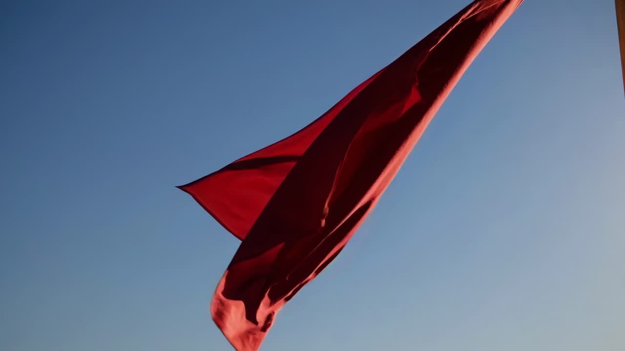 Dynamic low-angle shot of a red flag waving against a clear blue sky, capturing movement