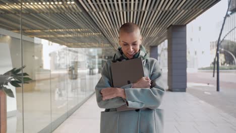 confident stylish professional female with shaved hair walking in outdoors office area with laptop. inspired marketing advertising creative business woman
