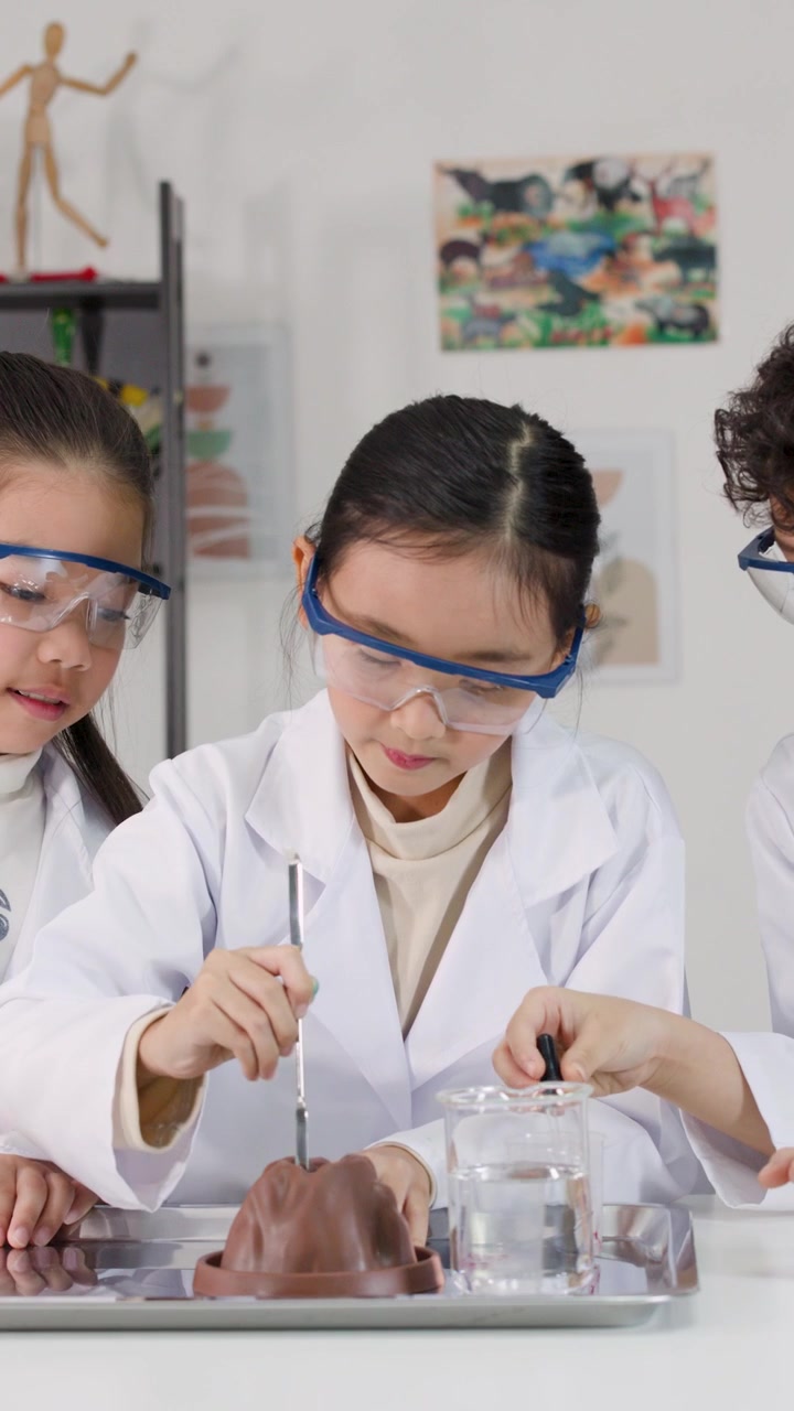 Anak-anak Asia mengenakan jas lab dan kacamata pengaman melakukan percobaan kimia di ruang kelas