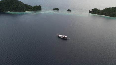 Beautiful-shot-of-Tropical-Island-with-stunning-phinisi-yacht-floating-above-the-calm-sea-in-Raja-Ampat-Indonesia