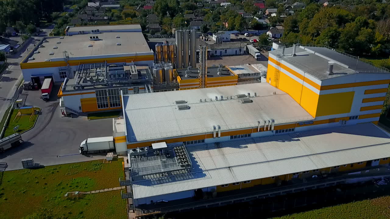 Territory of the plant with silver pipes. Private houses and green trees at backdrop. Aerial view.