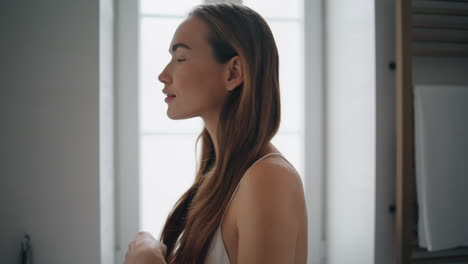 Modelo-Satisfecho-Cepillándose-El-Cabello-En-El-Primer-Plano-Del-Baño.-Tierna-Niña-Mirando-Cámara