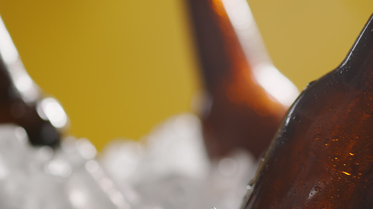 primer plano de una persona que toma una botella de vidrio refrigerada de cerveza fría o bebidas gaseosas de un cubo lleno de hielo contra un fondo amarillo 1