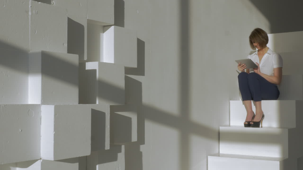 en el estudio una joven sentada en las escaleras y trabajando en la tableta