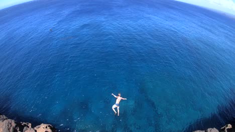 slow motion shot of a man doing a gainer off of a cliff at south point, big island, hawaii