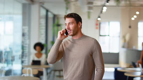 businessman standing in modern open plan office talking on mobile phone