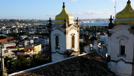 Vista-Aérea-De-La-Cima-De-La-Iglesia-Nosso-Senhor-Do-Bonfim,-La-Ciudad-Alrededor-Y-El-Océano-Al-Fondo,-Salvador,-Bahía,-Brasil