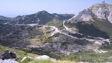 a spectacular scenic view from the njegos mausoleum, mount lovcen in montenegro, with vast green valleys between sharp mountain crests, small pine bush to the left, roads and trees below, pan 4k shot