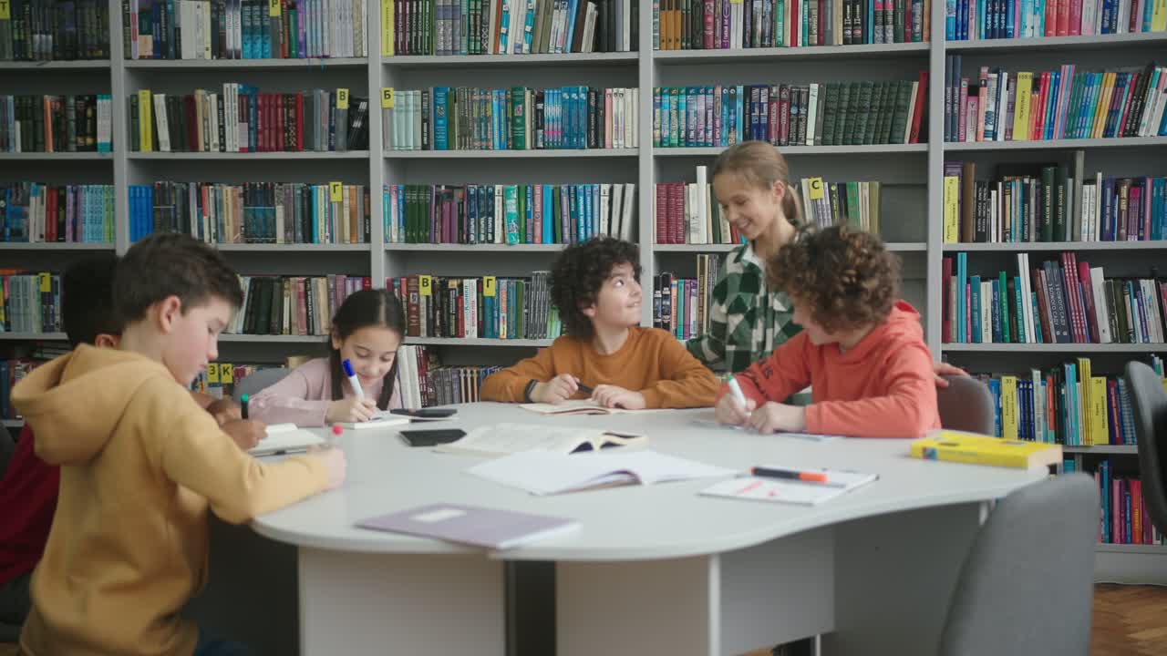 niños multinacionales se sientan en una mesa redonda en la biblioteca de la escuela