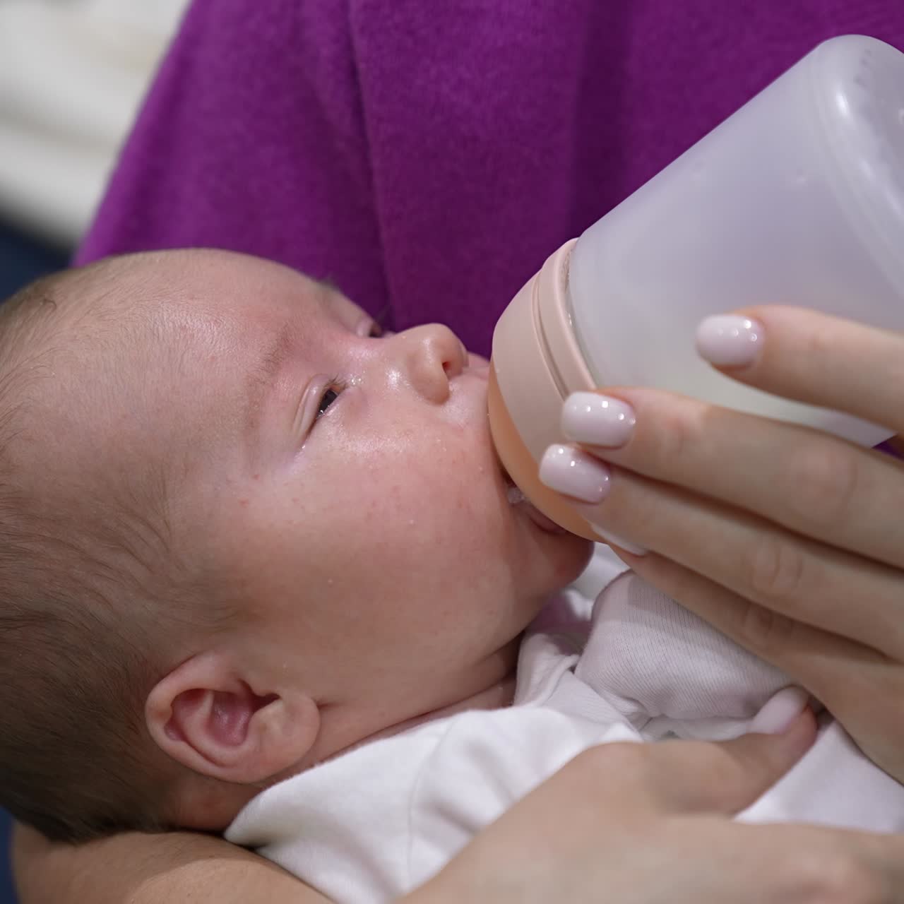 Mother is holding a child in her arms and feeding a baby from a bottle. Baby eating milk and falling asleep gradually. Close up