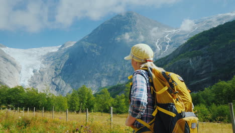 An-Active-Woman-With-A-Backpack-Walks-Against-The-Backdrop-Of-The-Mountains-And-The-Briksdal-Glacier