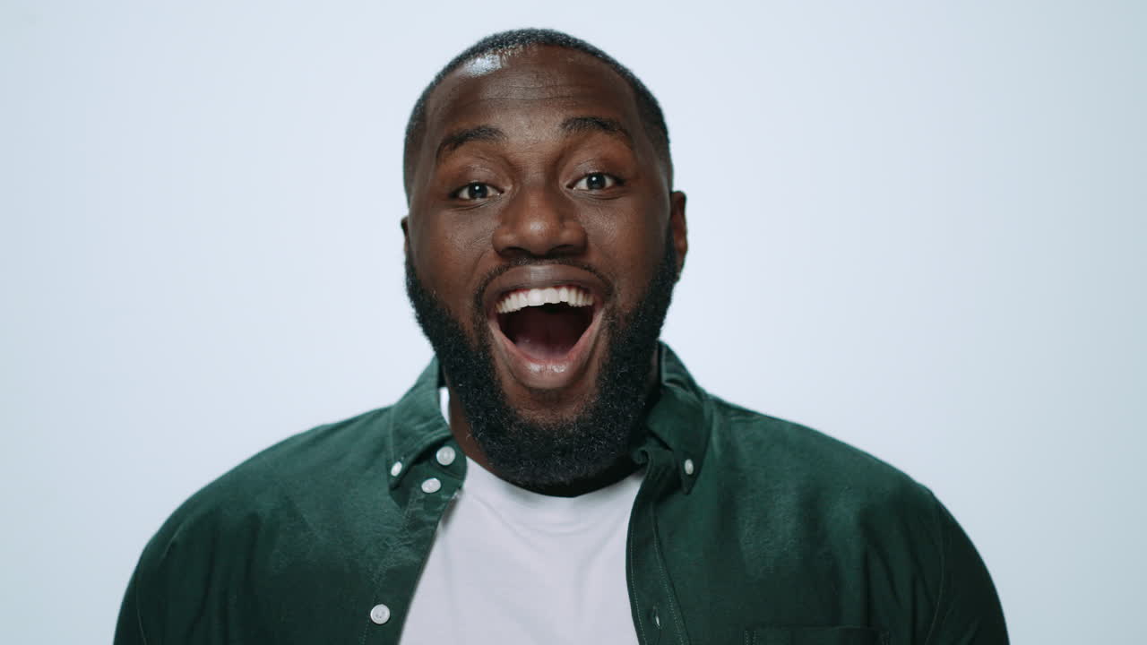 Portrait of surprised african guy covering mouth with hands in studio.