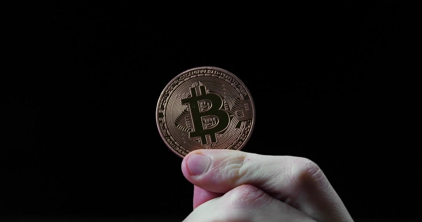 Siyah bir arka planın önünde bakır bir Bitcoin madeni parayı tutan yakın çekim.
