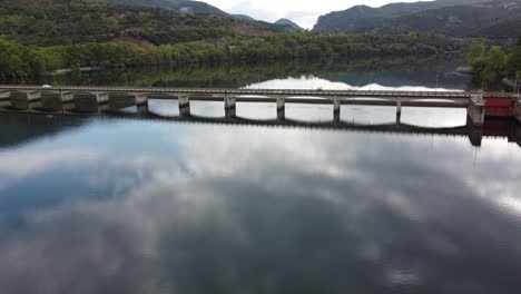 Toma-épica-De-Cine-Aéreo-De-Un-Automóvil-Que-Cruza-Un-Puente-Sobre-El-Río-Haliacmon-Aliakmonas-En-El-Norte-De-Grecia-Macedonia