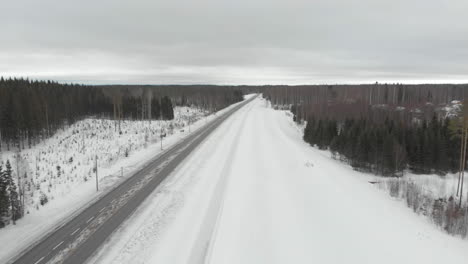 Aéreo,-Disparo-De-Drone,-Paralelo-A-La-Carretera-6,-Con-Vista-Al-Tráfico,-Rodeado-De-árboles-Sin-Nieve-Y-Sin-Hojas,-En-Un-Día-Nublado-De-Invierno,-En-Kontionlahti,-Pohjois-karjala,-Finlandia