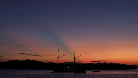 silueta de colinas y botes durante la puesta de sol con muchos zorros voladores o murciélagos en la isla kalong, labuan bajo indonesia