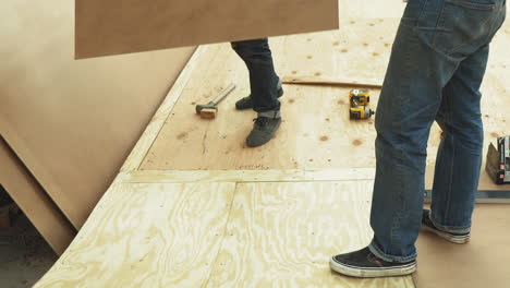 two men in jeans picking up plywood in workshop to build diy skateboard ramp, no face only legs, lower body