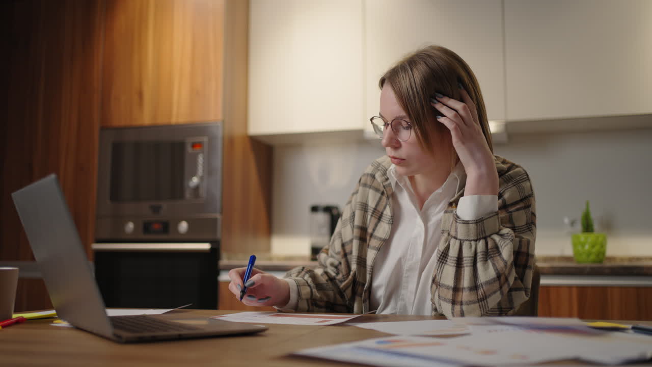 una mujer trabaja remotamente desde casa sentada en una mesa con una computadora portátil y un bolígrafo marca los datos en el gráfico. estudiante de aprendizaje a distancia en casa para realizar una tarea en economía