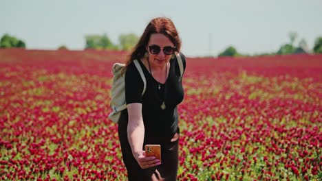 Middle-aged woman filming blooming clover flowers, peaceful countryside scene