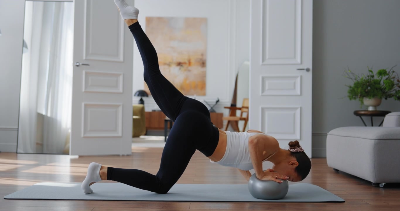 Young Woman Exercising with Small Pilates Ball at Home