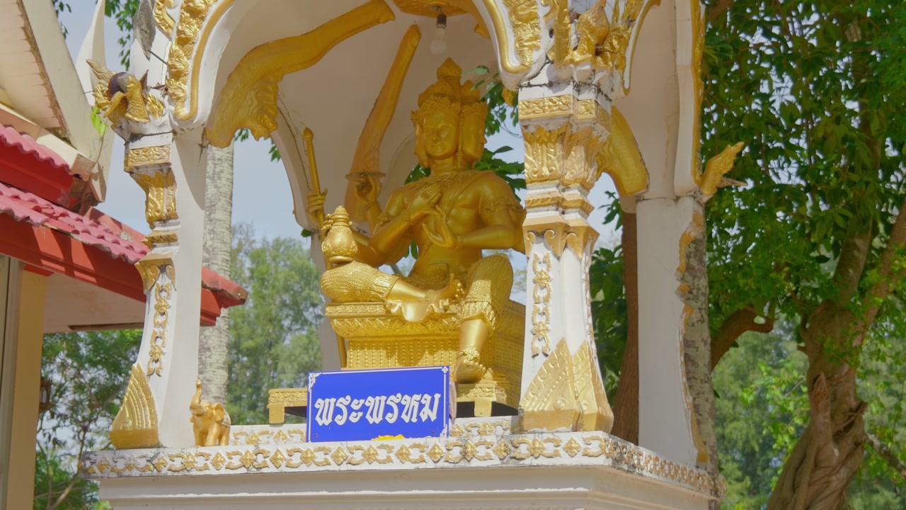 Close-up of a golden Phra Phrom (Brahma) statue with four faces inside an ornate white and gold shrine. Captured at Wat Nai Harn temple in Phuket, Thailand. 4K cinematic travel footage.