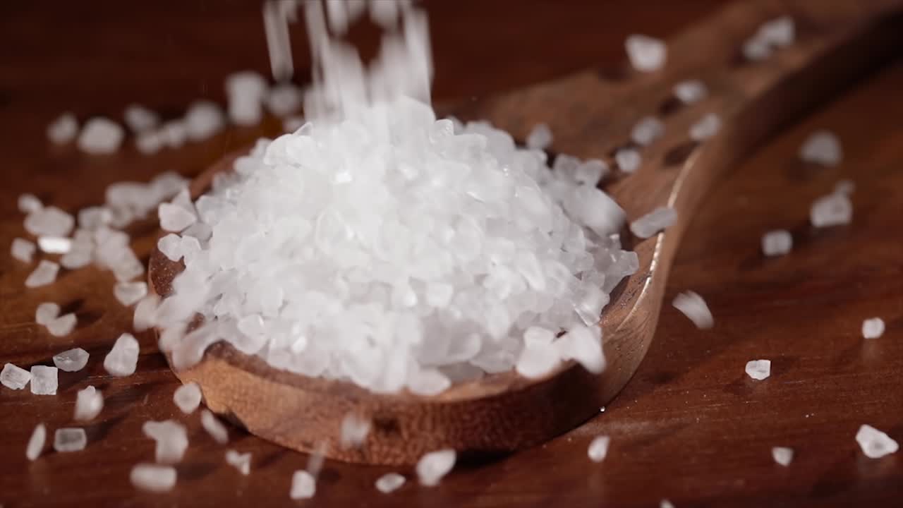 Sea salt crystals closeup in wooden spoon on a kitchen table.