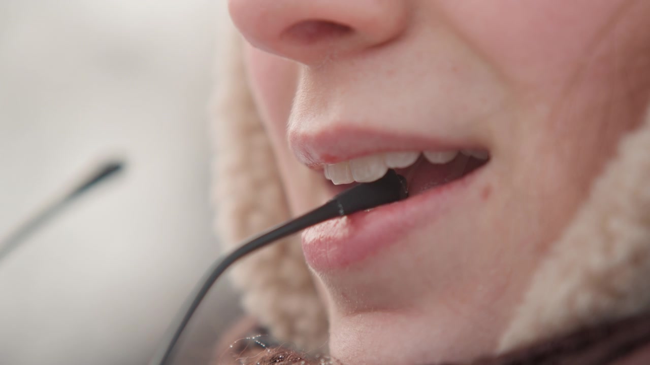 Tight side-front view shows lower face near microphone while lips move through speech and settle into slight smile, suggesting live interview or conversation in cold weather, with microphone, mouth