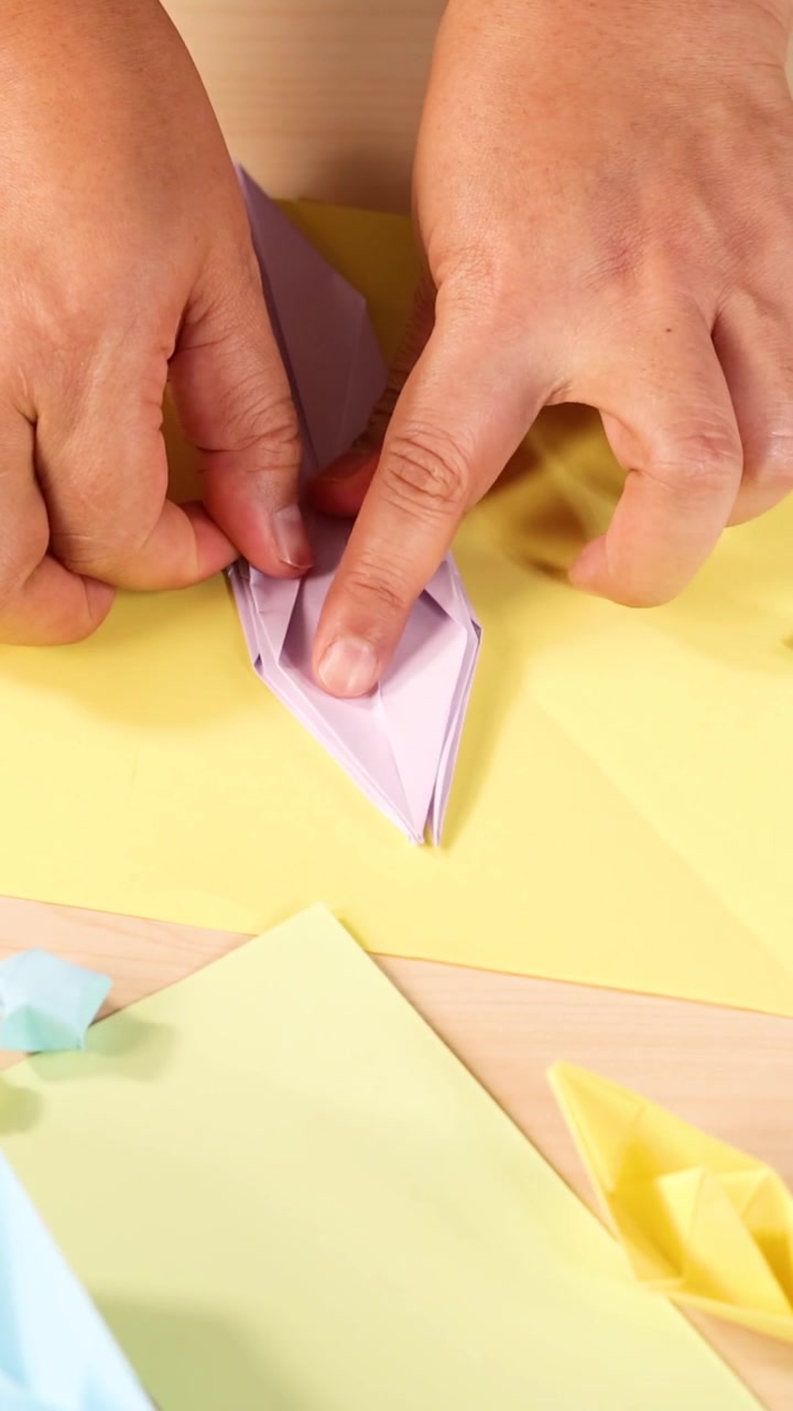 Close-up vertical shot of hands precisely folding purple paper into an origami crane shape.