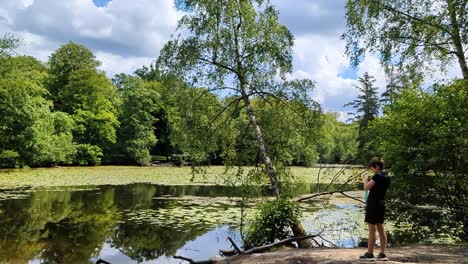4k 60fps jongen blaast zeepbellen op een prachtig meer in een deens bos, scandinavië, europa