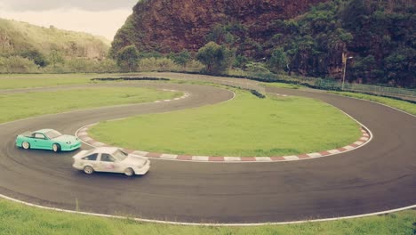 two high performance cars drifting or sliding around hairpin turn of race track