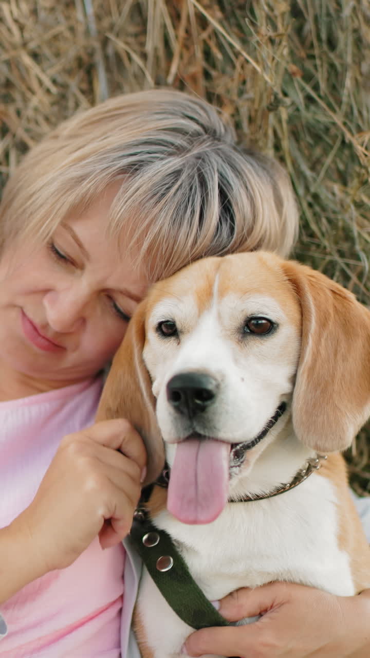 한 여인이 개를 가까이 붙잡고, 귀를 부드럽게 만지며, 광활한 농지에서  에 앉아있는 동안, 그녀는 개를 바라보고 머리에 머리를 습니다.
