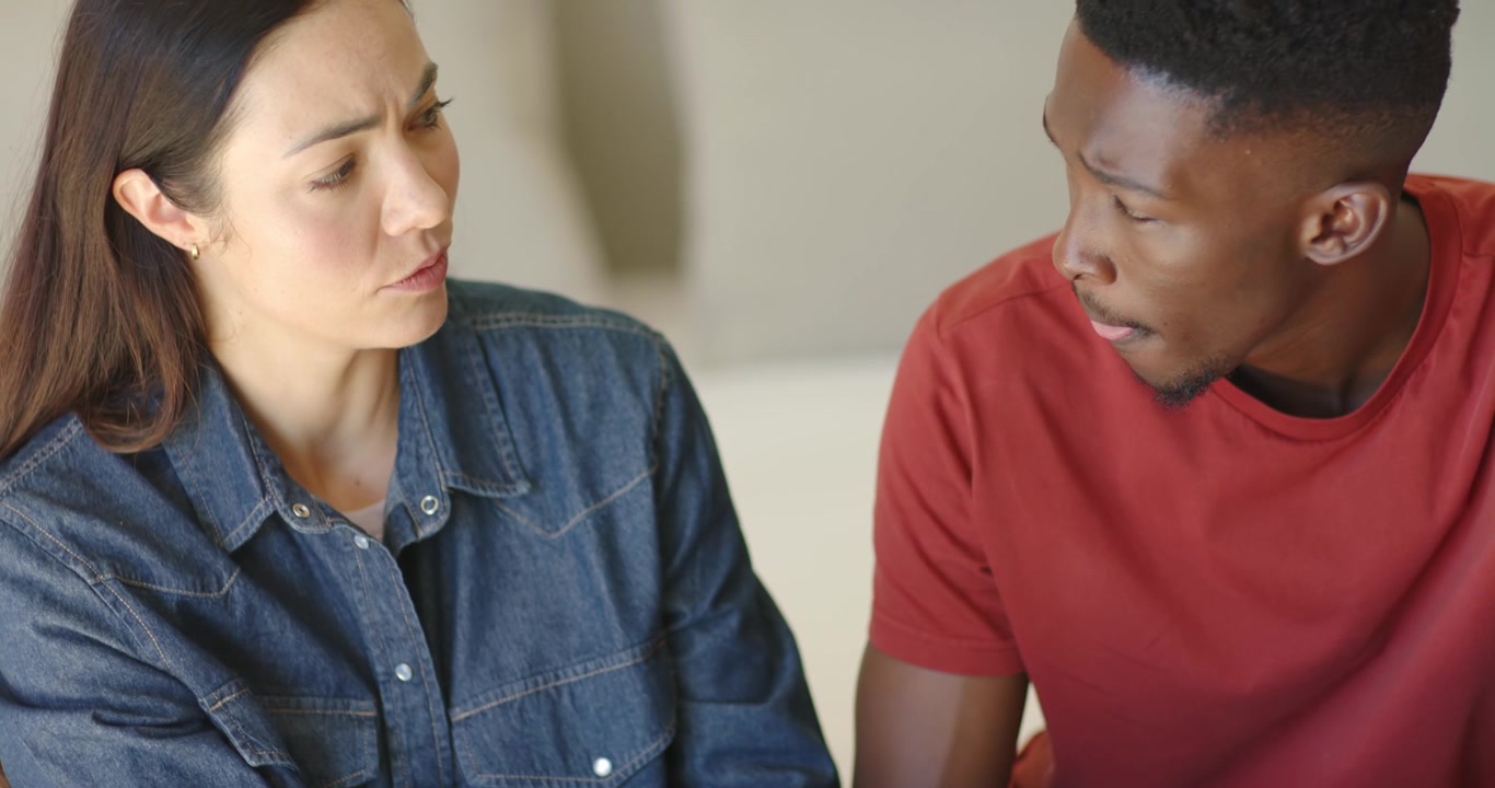 Asian woman initiating handhold and speaking for reassurance to African American man on sofa