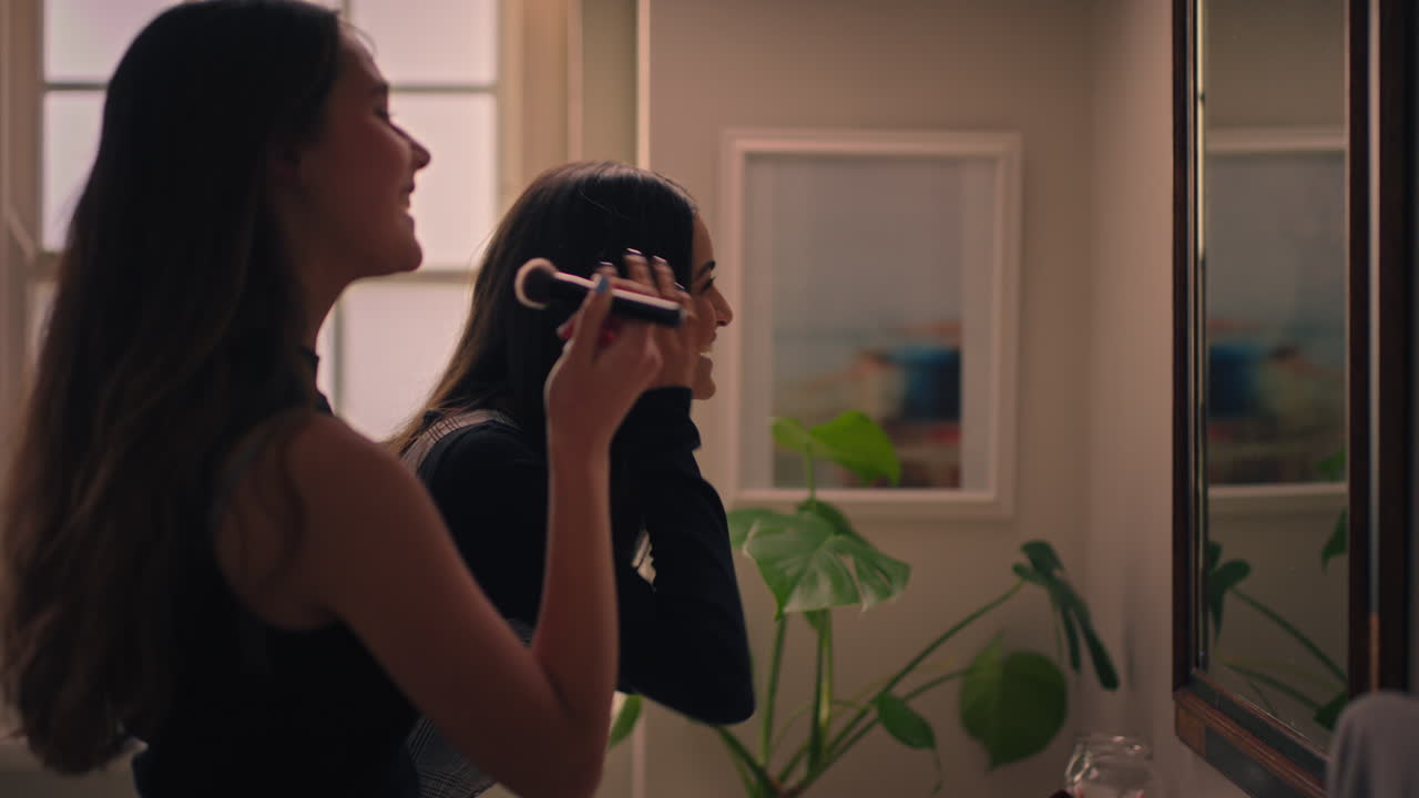 행복한 여자 친구들이 준비하고 거울을 보며 메이크업하는 십대들이 스타일리쉬한 패션을 입고 나갈 준비를 하고 있습니다.