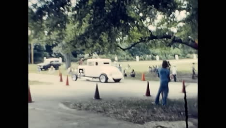 white truck driving down street surrounded by orange cones. circa usa - 1970s: a white truck drives down a street, navigating through orange cones in a vintage car show of the 1970s in the usa.