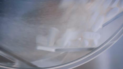 close up view of white pills in rotating container at pharmacy store