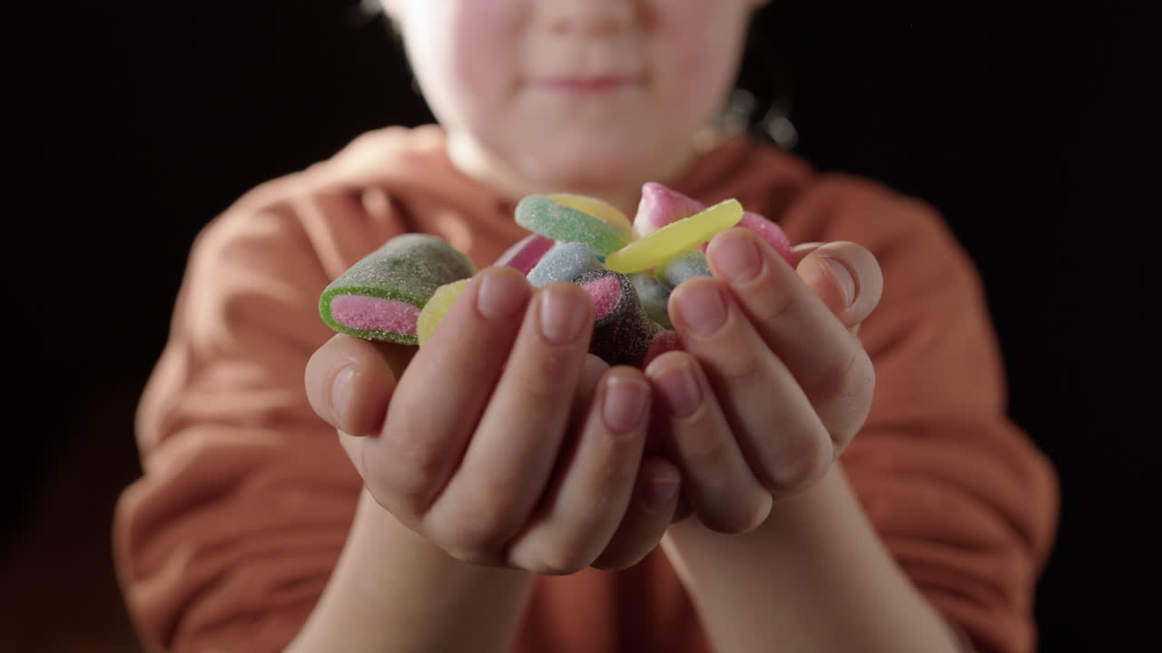 Boy holds out assorted sugary jelly sweets in cupped hands, temptation concept