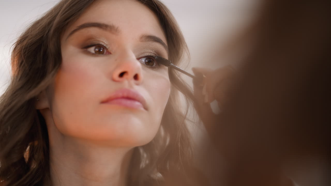 Focused woman applies mascara on lashes to accentuate look