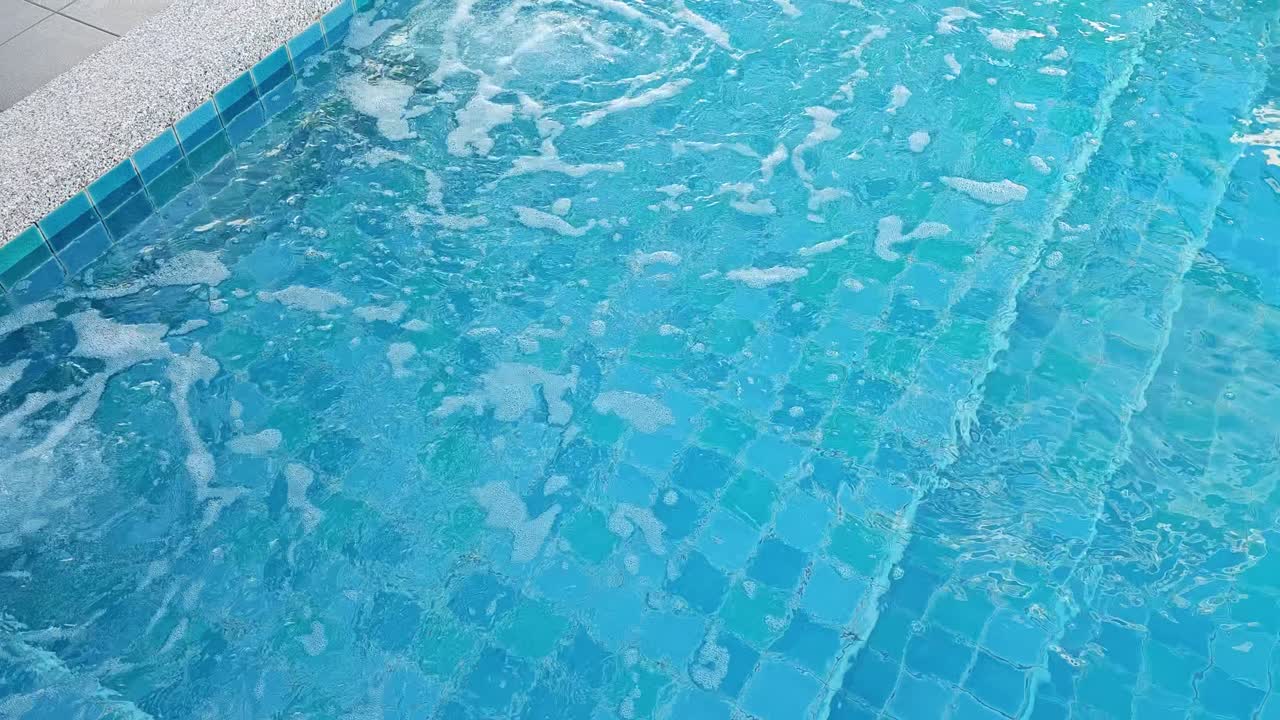 Pemandangan kolam renang yang tenang menampilkan percikan air biru cerah, cocok untuk bersantai.