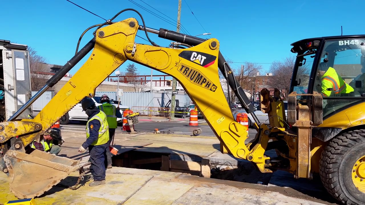 New York, USA, 9. marts 2022: Gul gravemaskine på vejarbejdsplads i New York. Rendegraver og arbejdere i sikkerhedsveste arbejder på reparation af byens gadeforsyning i New York.